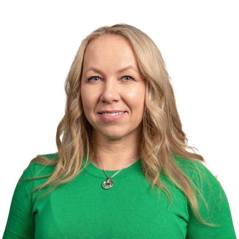 Smiling woman with blonde hair wearing a green sweater and a silver necklace, shown from the shoulders up.