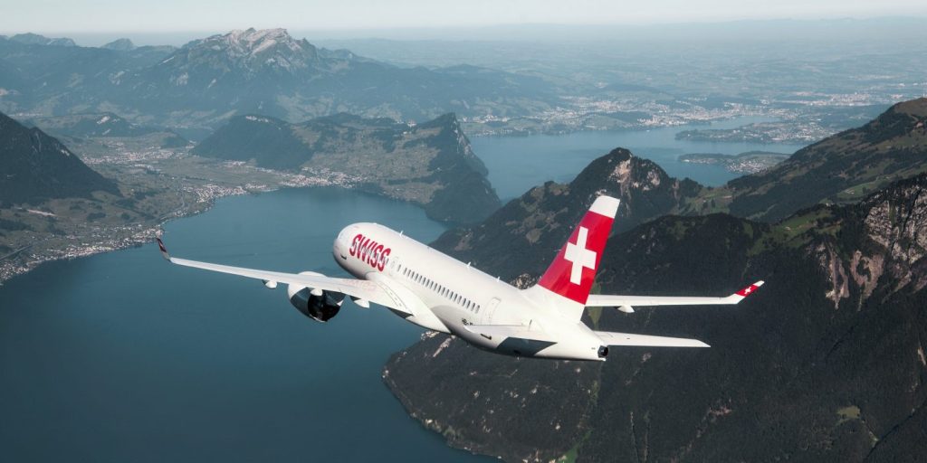 SWISS airliner soaring above a blue alpine lake with rugged Swiss Alps in the background.