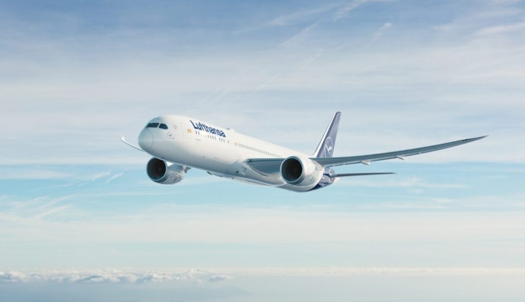 Lufthansa passenger jet flying above clouds in clear blue sky.