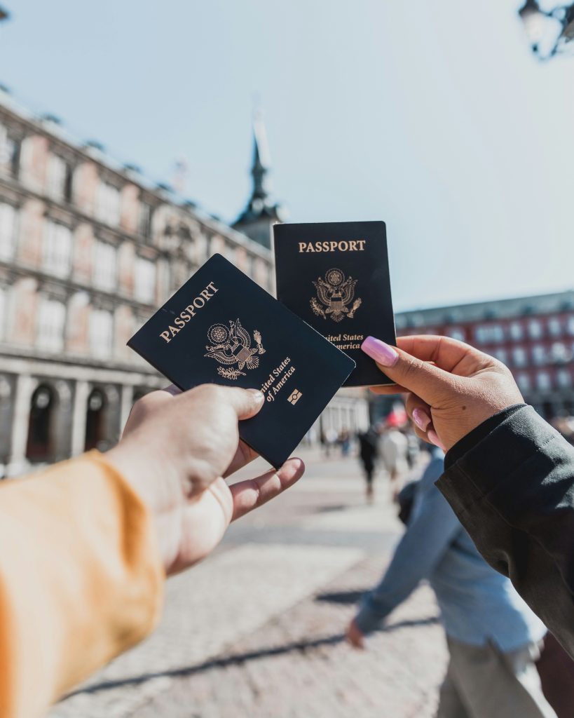Two hands hold dark-blue U.S. passports outdoors with a city street in the background.