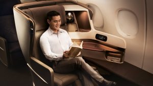 Man sitting in a premium airline business-class seat reading a book during travel.