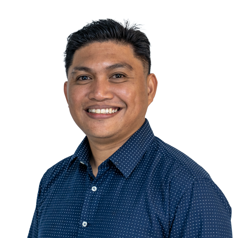 Smiling man with short black hair in a navy blue polka-dot shirt against a white background, facing slightly right.