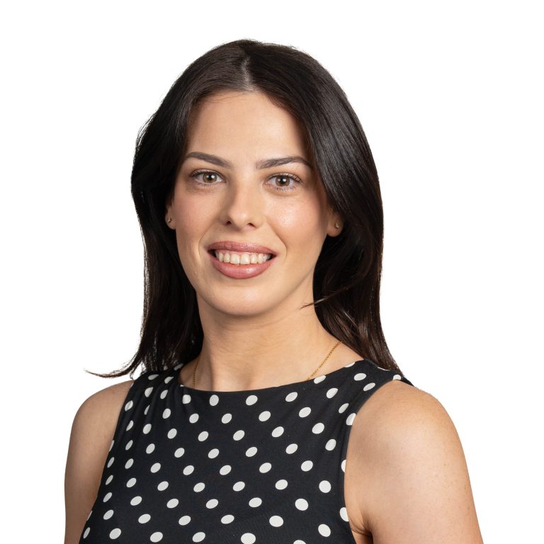 Smiling woman with dark hair wearing a navy polka-dot dress, cropped at shoulders against a white background.